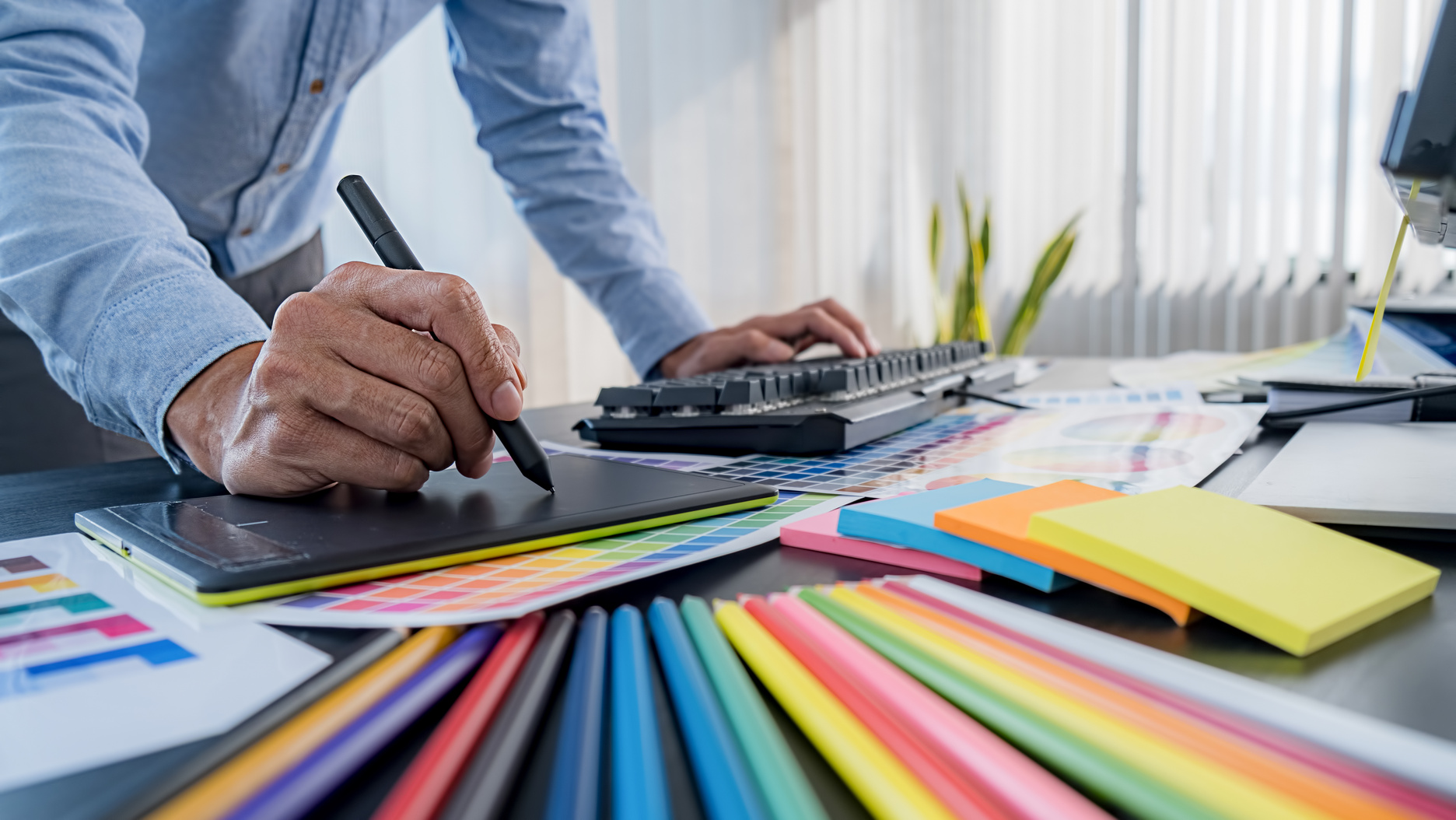 Graphic Designer Draws on Tablet next to Colored Palette 